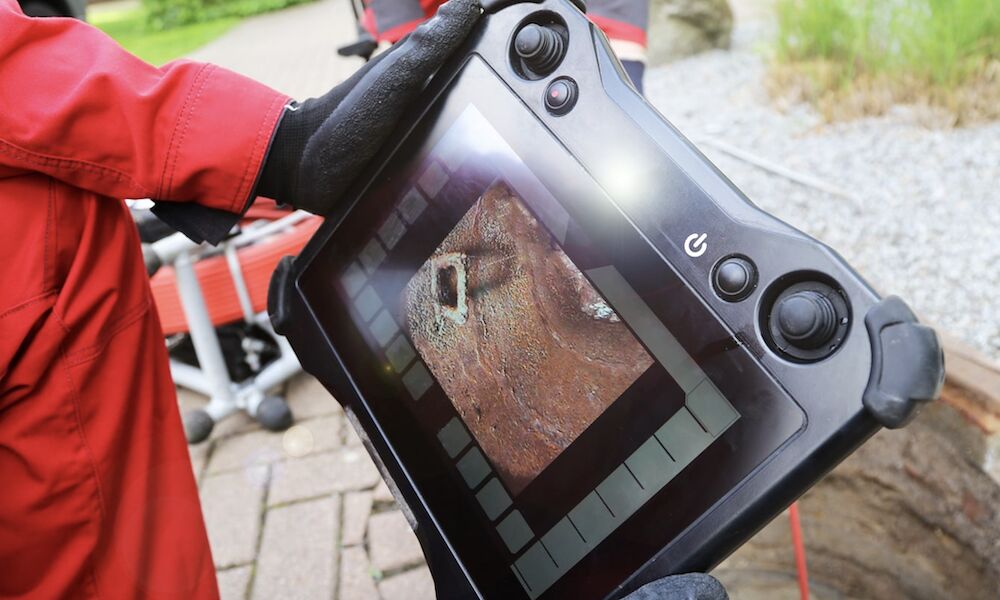 CCTV drain survey camera reel beside an open drain